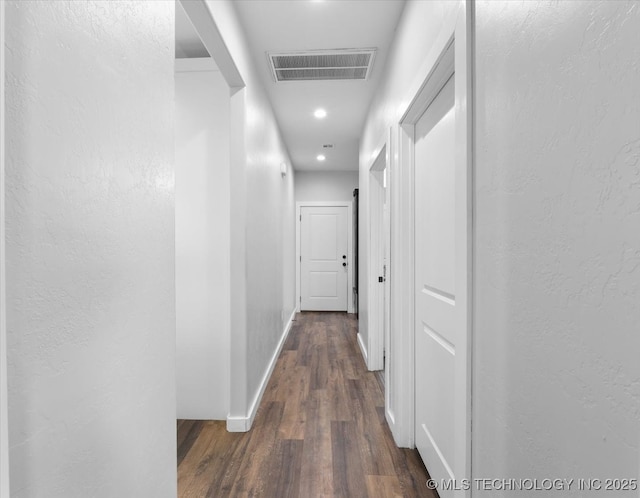 corridor with dark wood-style floors, baseboards, visible vents, and a textured wall