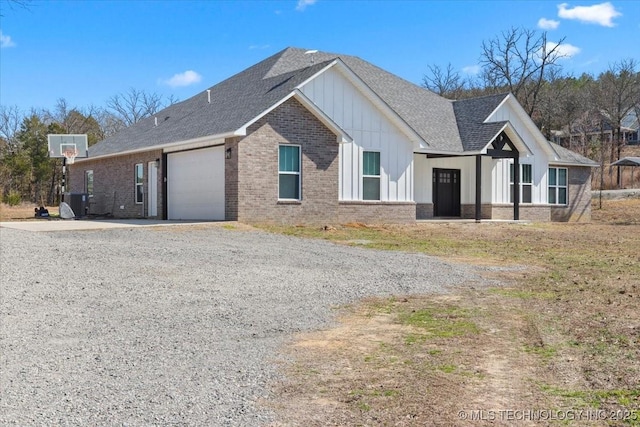 view of front of property featuring a garage, brick siding, a shingled roof, board and batten siding, and gravel driveway