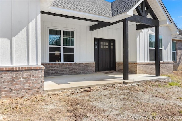 view of exterior entry featuring brick siding and roof with shingles