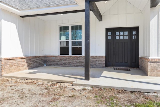 property entrance with a shingled roof, brick siding, and board and batten siding