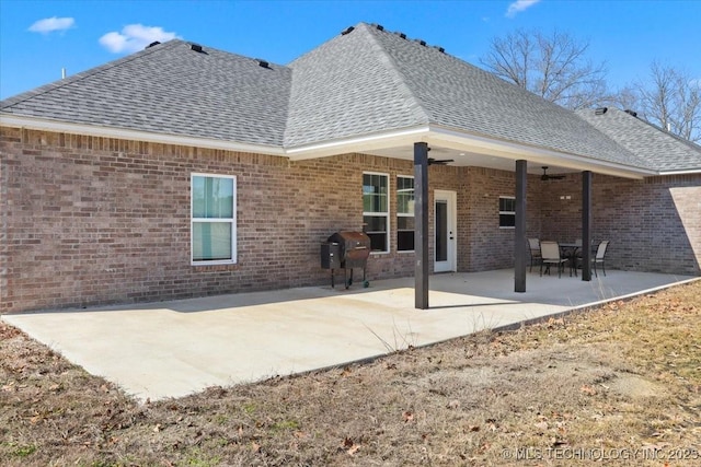 back of house with brick siding, roof with shingles, a patio area, and a ceiling fan