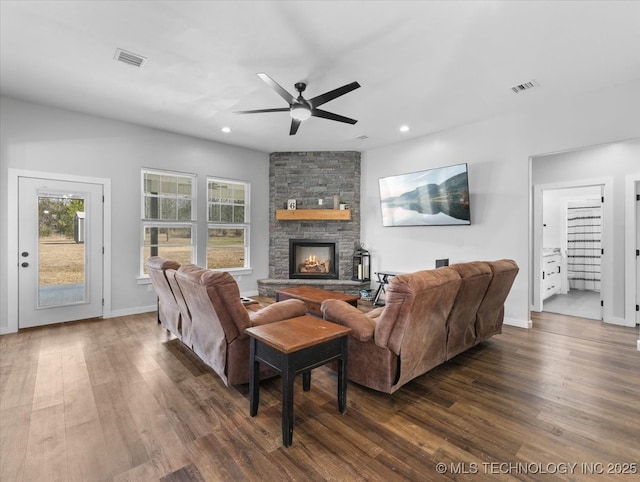 living area featuring recessed lighting, visible vents, dark wood-style flooring, and a stone fireplace