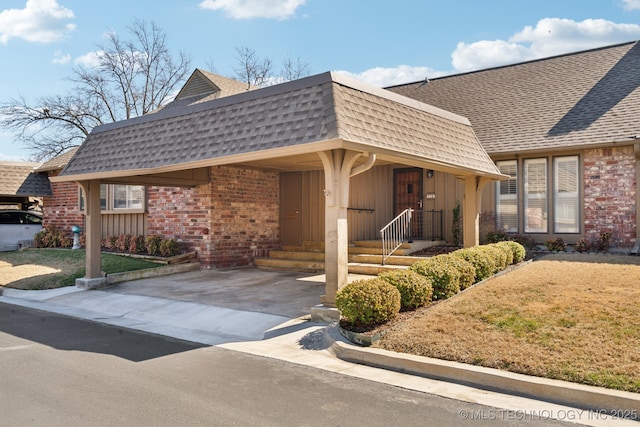 view of front of house with brick siding, an attached carport, mansard roof, and a shingled roof