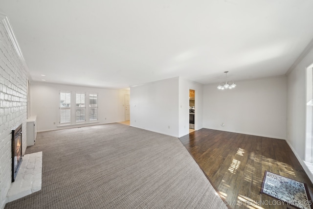 living area with a chandelier, ornamental molding, a brick fireplace, and dark wood-style flooring