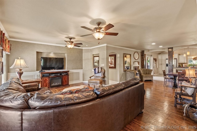 living room with arched walkways, wainscoting, a glass covered fireplace, hardwood / wood-style floors, and crown molding