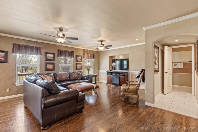 living room featuring baseboards, arched walkways, ceiling fan, ornamental molding, and wood finished floors