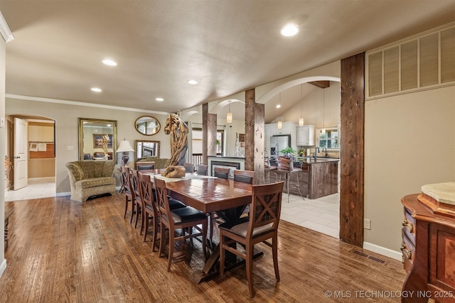 dining area with arched walkways, vaulted ceiling, and wood finished floors