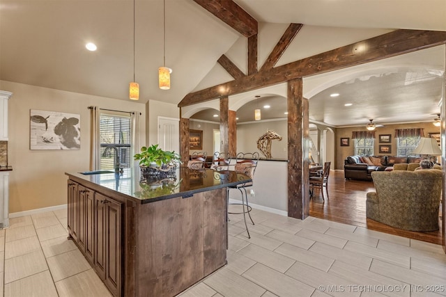 kitchen featuring arched walkways, beamed ceiling, dark countertops, and a sink