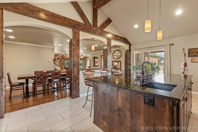 kitchen with arched walkways, a sink, lofted ceiling with beams, and dark stone countertops