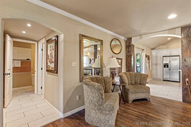 sitting room with arched walkways, baseboards, vaulted ceiling, light wood-style floors, and ornamental molding