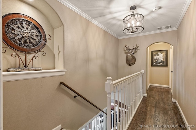 corridor with dark wood finished floors, crown molding, visible vents, an upstairs landing, and baseboards