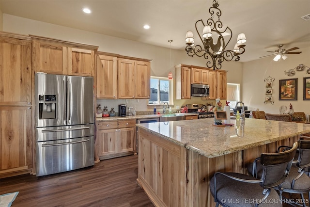 kitchen featuring light stone counters, dark wood-type flooring, a kitchen island, appliances with stainless steel finishes, and a kitchen bar