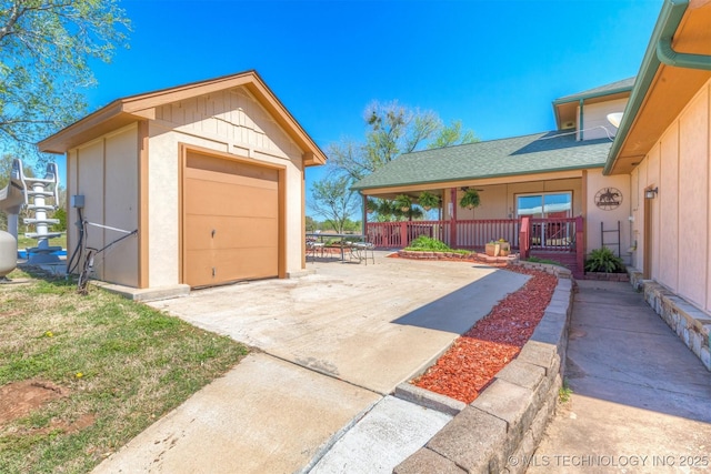 detached garage with driveway, a porch, and fence