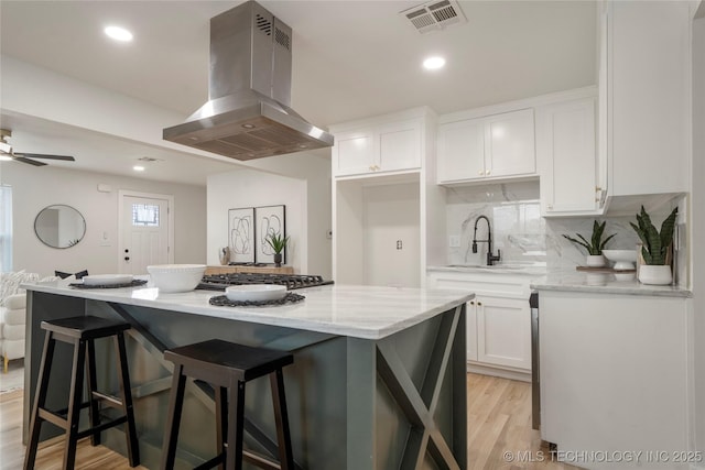 kitchen featuring a sink, visible vents, white cabinetry, light wood-type flooring, and island exhaust hood