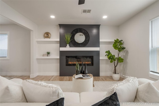 living area featuring a large fireplace, visible vents, plenty of natural light, and wood finished floors