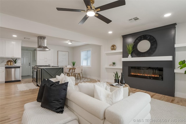 living area featuring light wood-style flooring, a fireplace, visible vents, and baseboards