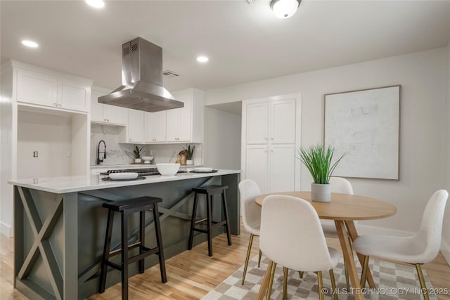 kitchen with island exhaust hood, decorative backsplash, white cabinets, and light countertops