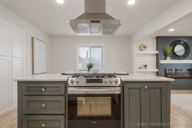 kitchen with stainless steel gas range oven, a glass covered fireplace, wall chimney exhaust hood, light stone counters, and light wood-type flooring