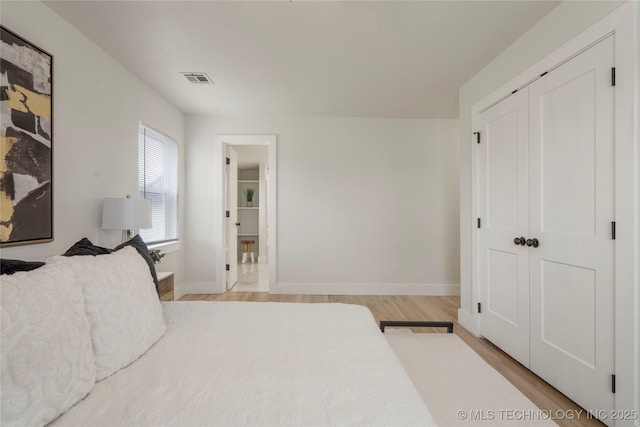 bedroom featuring a closet, baseboards, visible vents, and light wood finished floors