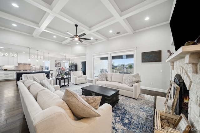 living area featuring visible vents, dark wood-type flooring, a stone fireplace, coffered ceiling, and beamed ceiling