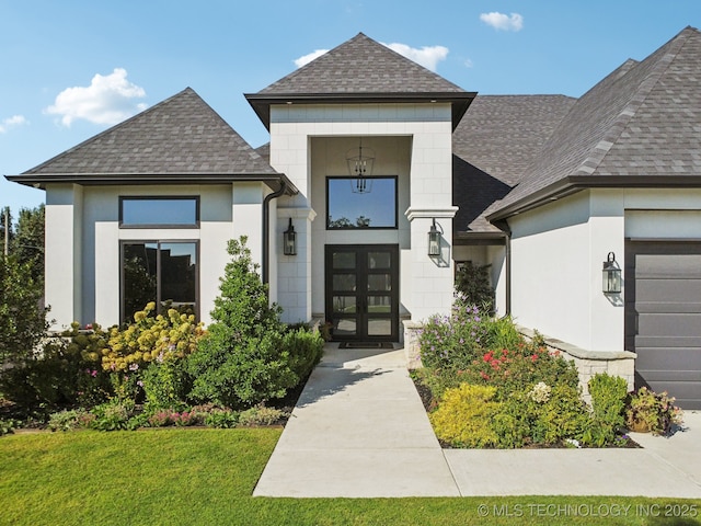 doorway to property featuring a garage, a yard, roof with shingles, and stucco siding