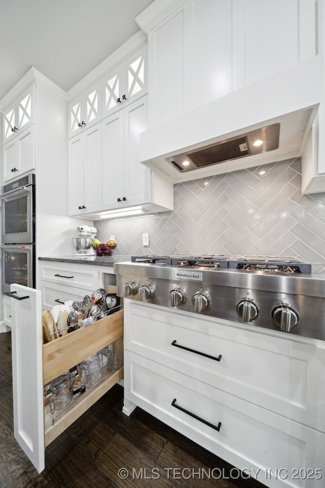 kitchen with tasteful backsplash, custom range hood, appliances with stainless steel finishes, glass insert cabinets, and white cabinetry