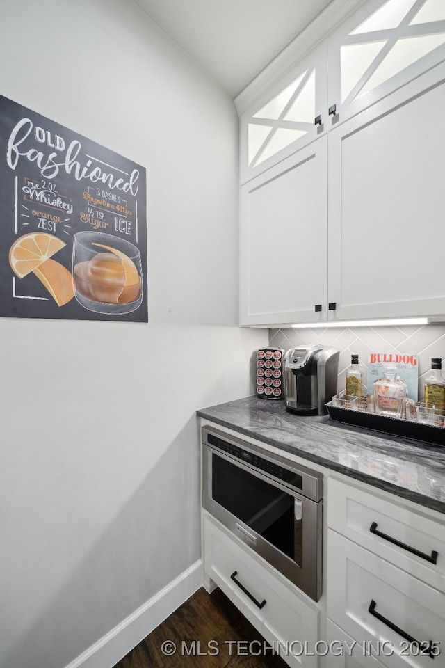 interior space with stainless steel microwave, white cabinetry, and decorative backsplash