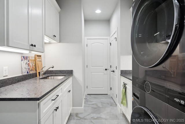 washroom with stacked washer and dryer, a sink, baseboards, marble finish floor, and cabinet space