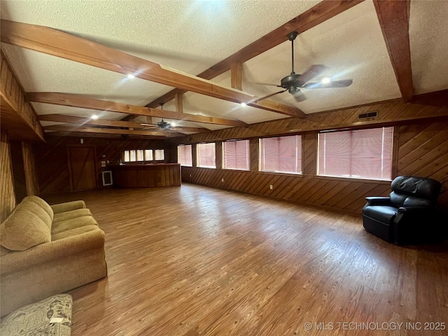 living area with ceiling fan, wood walls, a textured ceiling, and light wood-style flooring