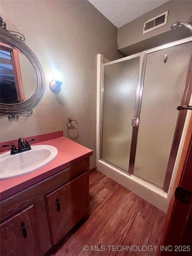 bathroom featuring visible vents, wood finished floors, a textured ceiling, vanity, and a shower stall