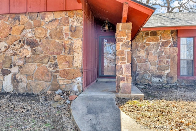 view of exterior entry featuring stone siding and roof with shingles