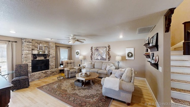 living area featuring a fireplace, visible vents, a textured ceiling, wood finished floors, and stairs