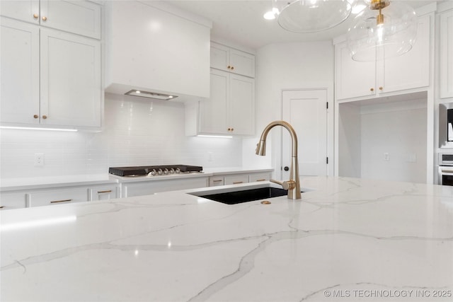 kitchen with white cabinets, a sink, light stone countertops, stovetop, and backsplash