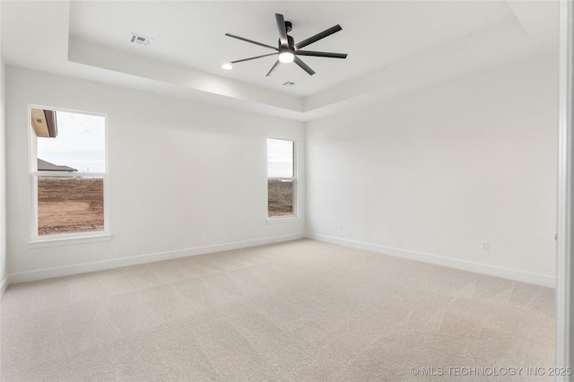 empty room with baseboards, a tray ceiling, and light colored carpet