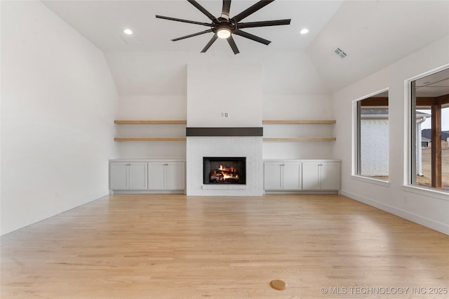 unfurnished living room featuring light wood-type flooring, a warm lit fireplace, visible vents, and lofted ceiling