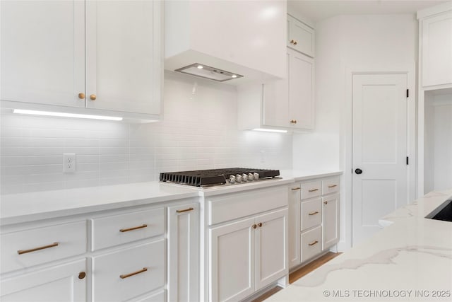 kitchen featuring stainless steel gas cooktop, custom exhaust hood, decorative backsplash, white cabinets, and light stone countertops