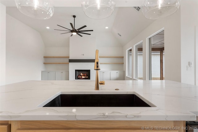 kitchen with visible vents, a glass covered fireplace, open floor plan, vaulted ceiling, and a sink