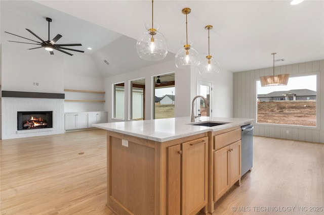 kitchen with a sink, a ceiling fan, open floor plan, a lit fireplace, and light wood finished floors