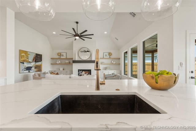 kitchen featuring visible vents, open floor plan, light stone counters, and a sink