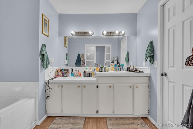 bathroom with double vanity, wood finished floors, tiled bath, and a sink