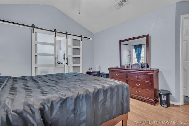 bedroom featuring lofted ceiling, light wood-type flooring, a barn door, and visible vents