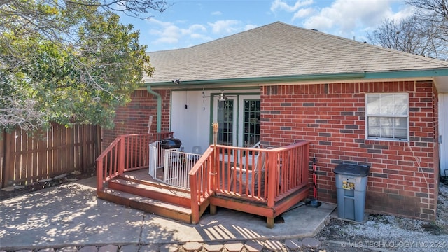 rear view of house with brick siding, a shingled roof, fence, and a wooden deck