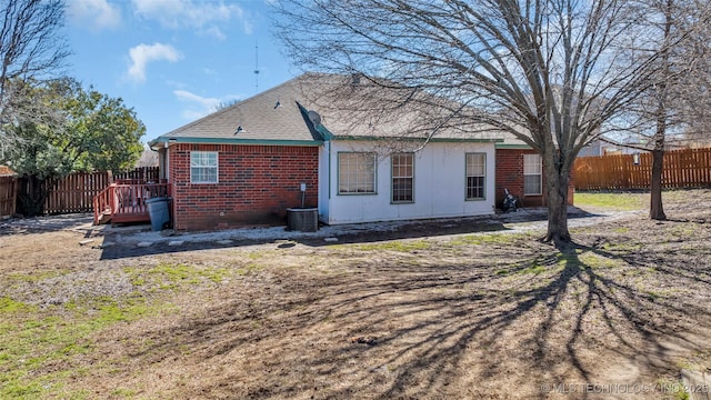 rear view of house with a deck, central AC, brick siding, and a fenced backyard