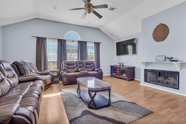 living area with a glass covered fireplace, visible vents, vaulted ceiling, and wood finished floors