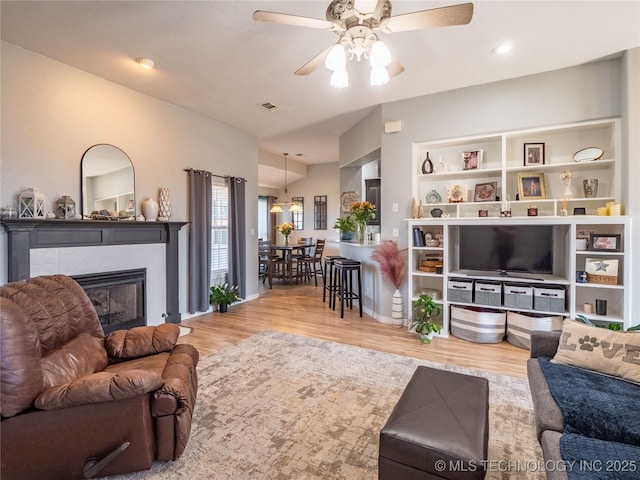 living area featuring wood finished floors, baseboards, a fireplace, ceiling fan, and vaulted ceiling