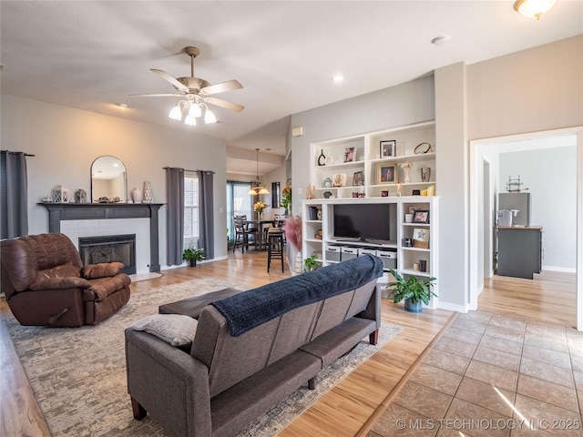 living area with a tiled fireplace, baseboards, light wood finished floors, and ceiling fan