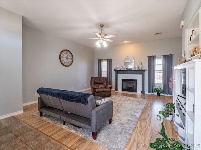 living room with wood finished floors, baseboards, visible vents, a fireplace with flush hearth, and ceiling fan