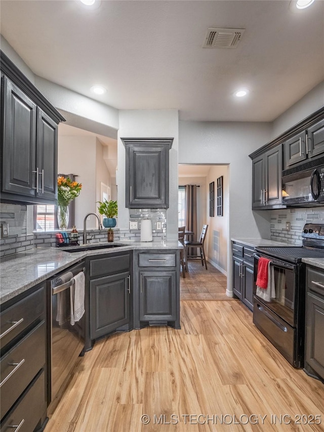 kitchen featuring visible vents, light wood-type flooring, decorative backsplash, black appliances, and a sink