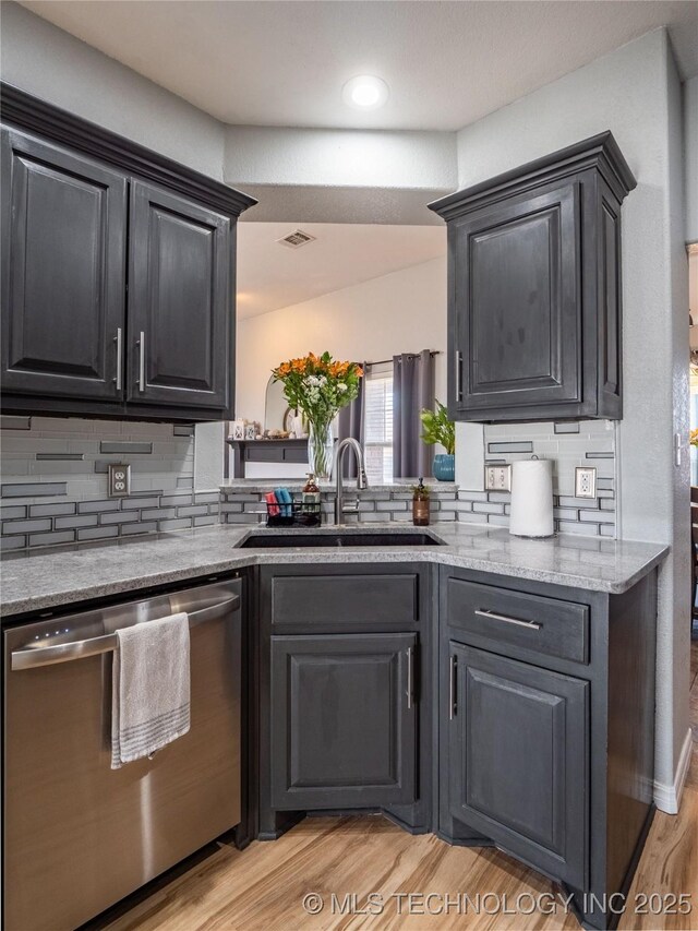 kitchen with a sink, tasteful backsplash, light wood-style floors, and dishwasher