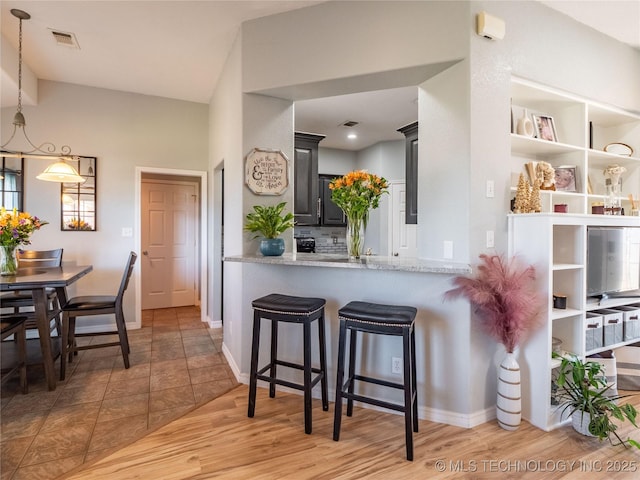 kitchen with visible vents, baseboards, light wood-type flooring, a kitchen bar, and light stone counters